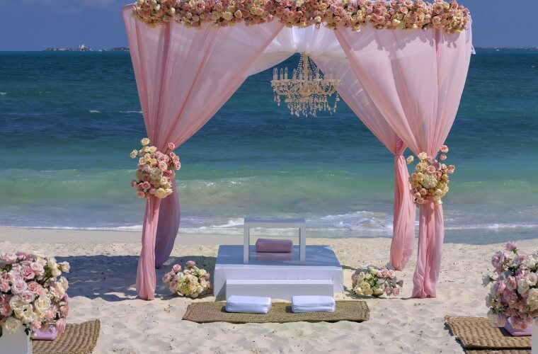 beach silk ceremony setup with a pink decorated wedding arch 