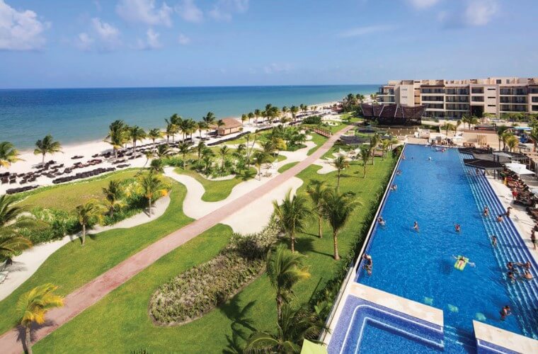 the pool and gardens at Royalton Riviera Cancun with palm trees on the beach in the background 