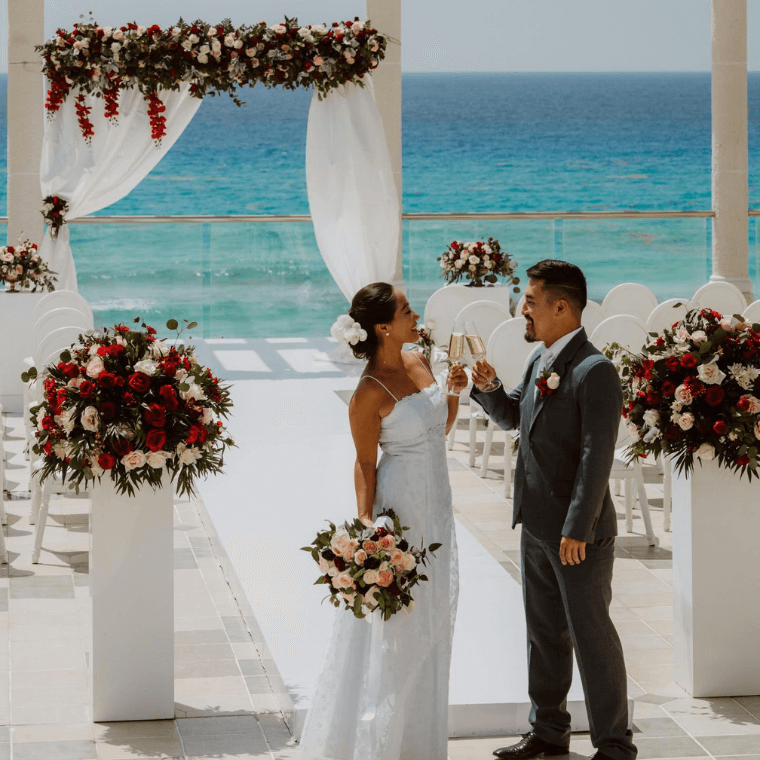 a wedding couple toasting each other with a wedding arch and the Caribbean Sea in the background 
