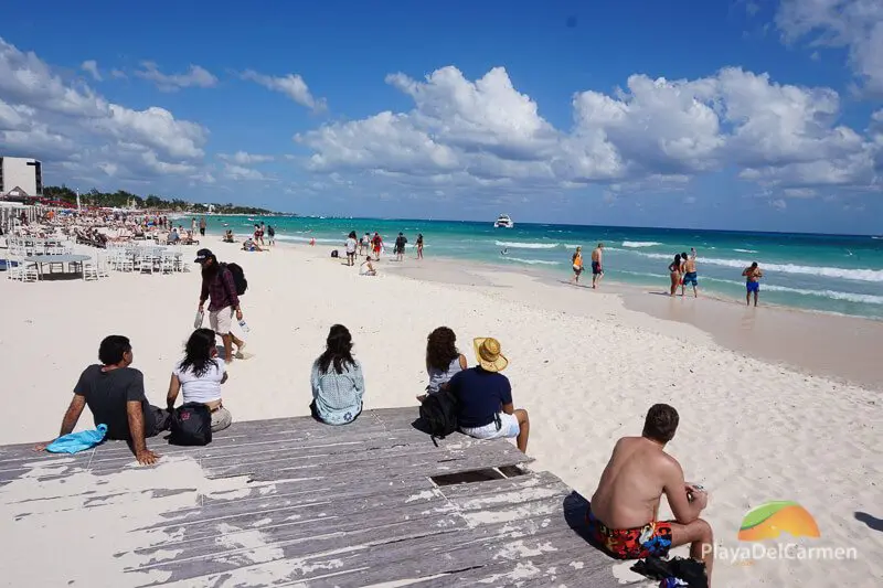 People sit on a wooden platform overlooking the Caribbean Sea at a Playa del Carmen beach