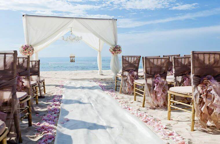 beach wedding setup at El Dorado Seaside palms with decorated chairs and a wedding arch 
