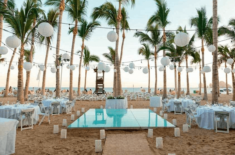 beach wedding setting with palm trees and a white covered altar and tables 