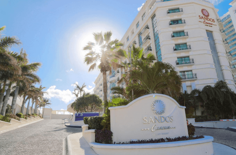 front of Sandos Cancun with the name sign and palm trees 
