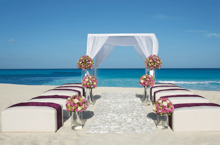 beach wedding setup at Secrets the Vine Cancun with a wedding arch and decorated with pink and white flowers 