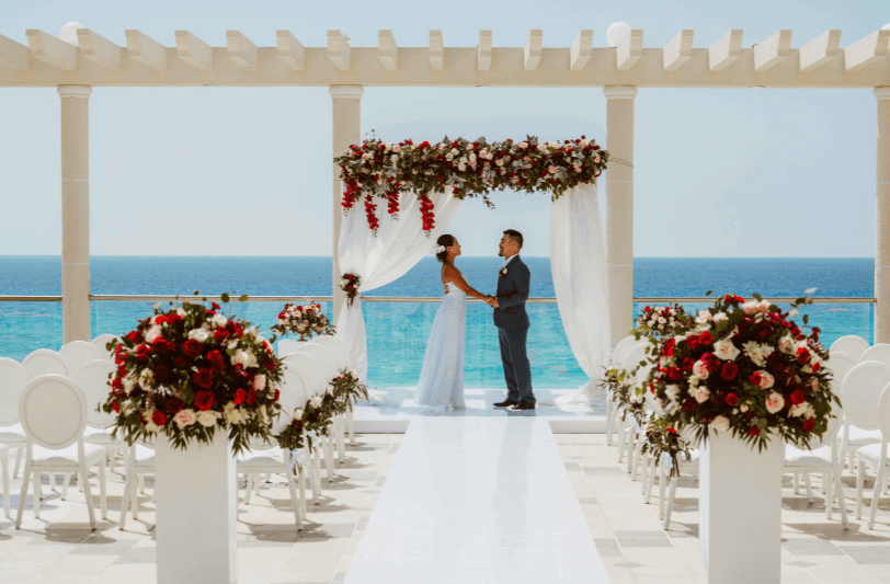 a couple stood facing each other under a decorated wedding arch with the Caribbean Sea in the background