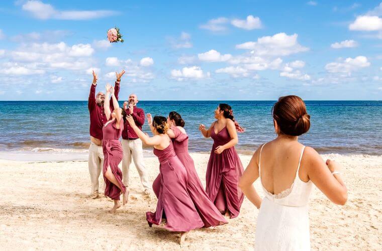 a bride throwing her bouquet to members of the wedding party on the beach 