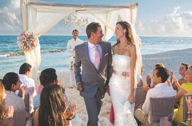 bride and groom walking down a beach aisle passing their wedding guests after getting married 