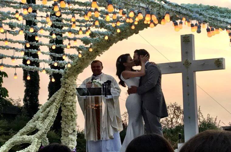 Eva Longoria and Jose Baston kissing with the wedding officiant and a cross in the background