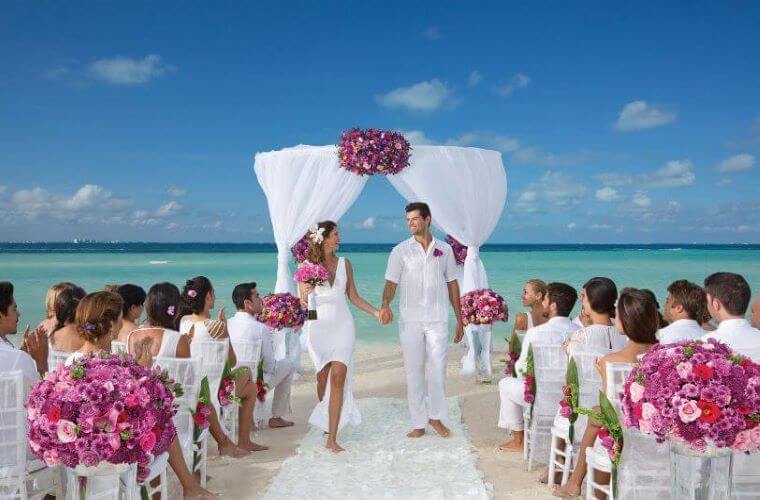 a couple running past their guests hand in hand after a beach wedding ceremony