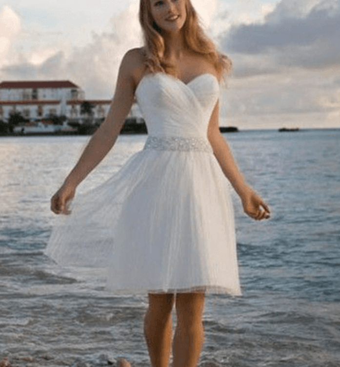a girl in a short white wedding dress walking on a beach