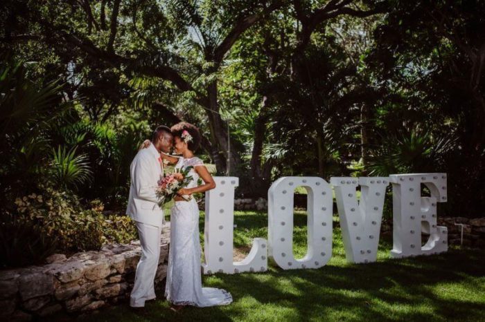 a wedding couple in a garden next to a big statue of the word love