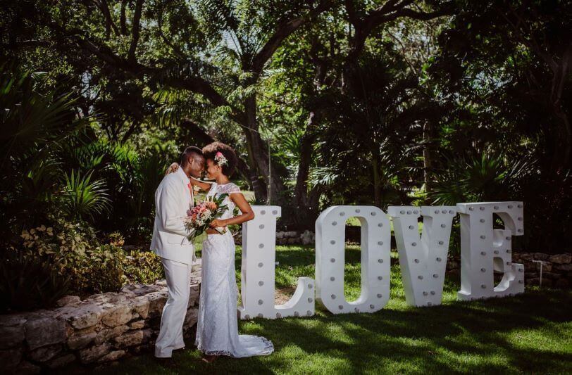 a wedding couple in a garden next to a big statue of the word love