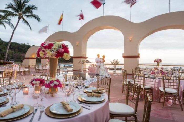 a wedding couple in the background with circular tables in the foreground set for a destination wedding