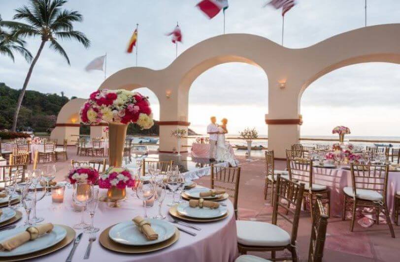 a wedding couple in the background with circular tables in the foreground set for a destination wedding