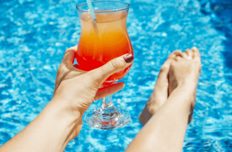 a woman's hand holding a cocktail while she is in the pool 