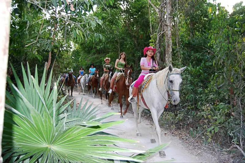 A group rides horses through the Riviera Maya jungle
