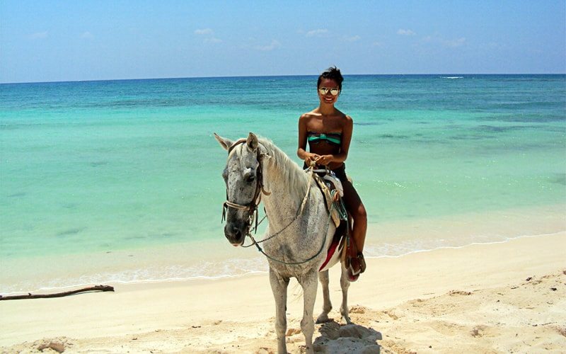 A woman on a white horse with the turquoise colors of the Caribbean Sea in the background