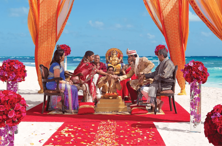 six people taking part in an Indian wedding ceremony on the beach at Dreams Playa Mujeres