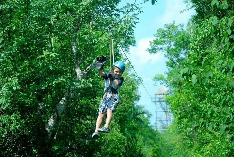 Kid waves at the camera while zip lining through the Riviera Maya jungle