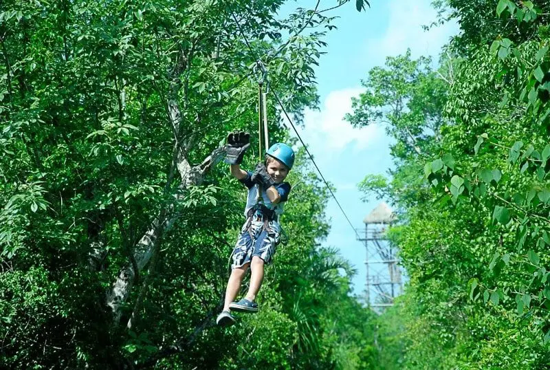 A boy waves as he zip lines through the jungle outside of Playa del Carmen, Mexico