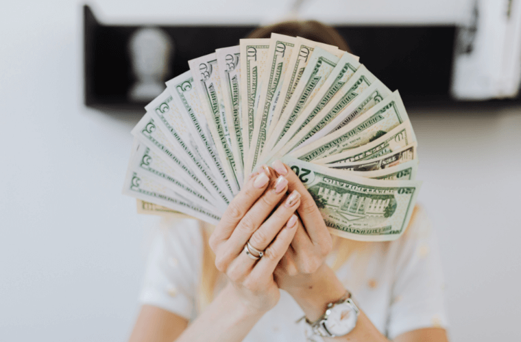 a woman holding dollars that are fanned out to hide her face