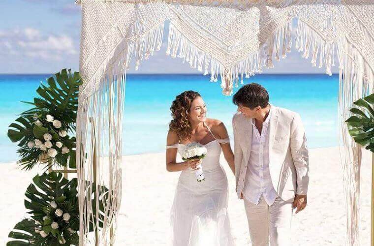 a wedding couple dressed in white walking away from the Caribbean Sea 