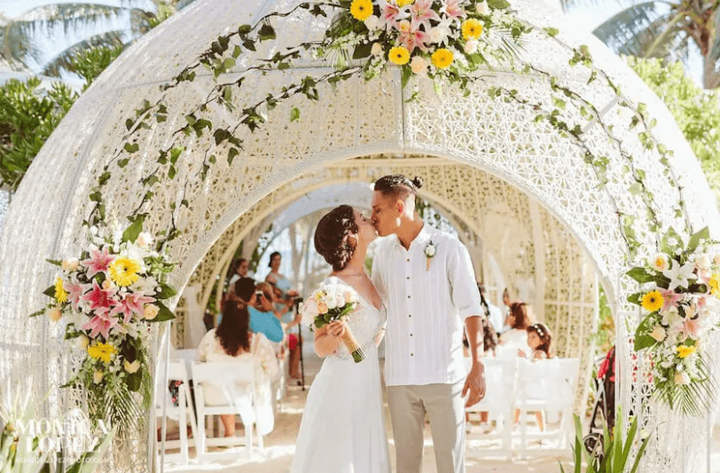 A wedding couple kissing in front of an archway