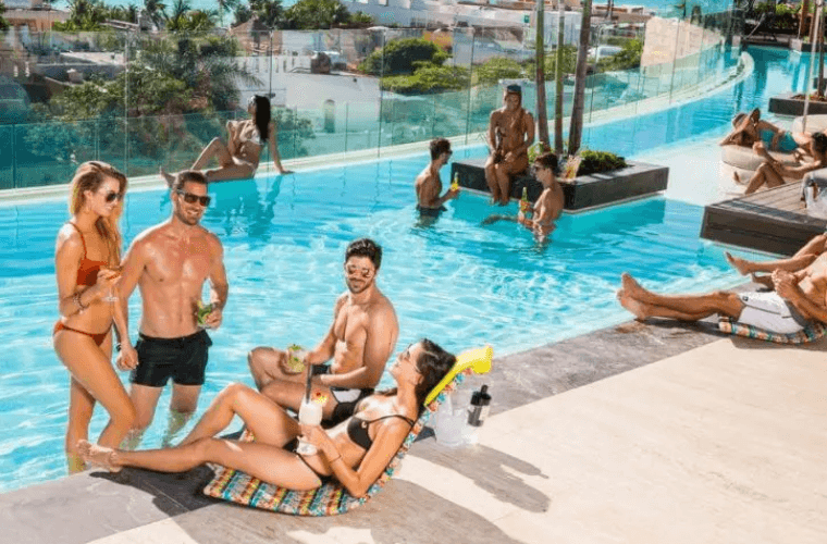 men and women wearing trunks and bikinis relaxing next to and in a pool