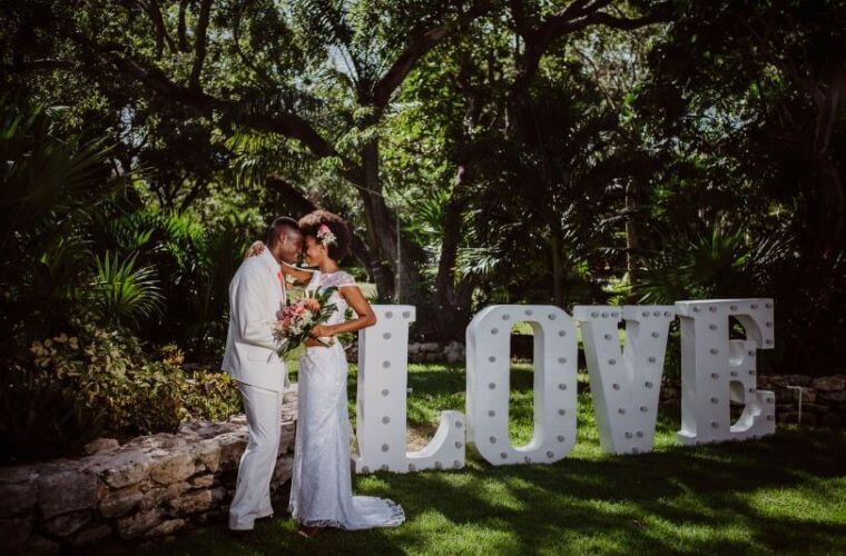 a wedding couple with a large freestanding love sign in a garden location