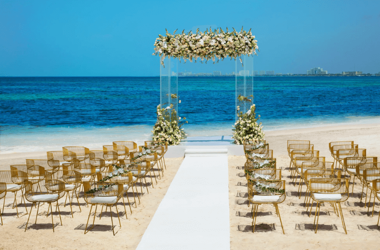 the beach wedding setup at Dreams Vista Cancun with a wedding arch decorated with flowers and chairs for guests