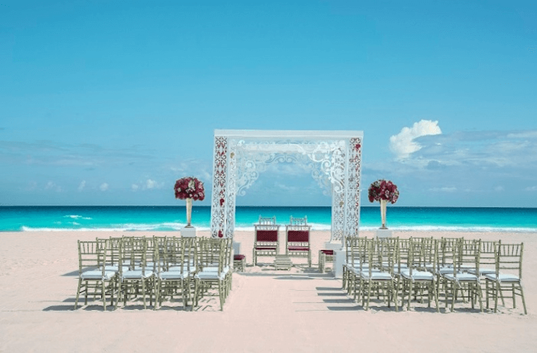 beach wedding setup at Iberostar Selection Cancun with a decorated square wedding arch and chairs for the guests 