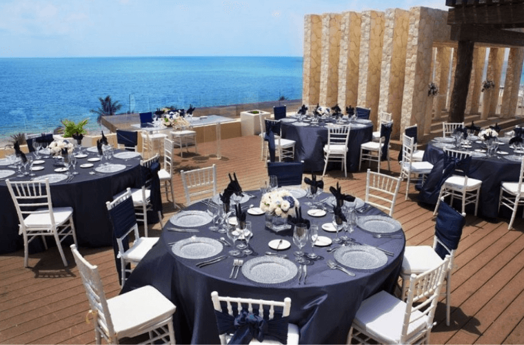 large round tables with blue coverings set for a wedding with views of the Caribbean Sea 