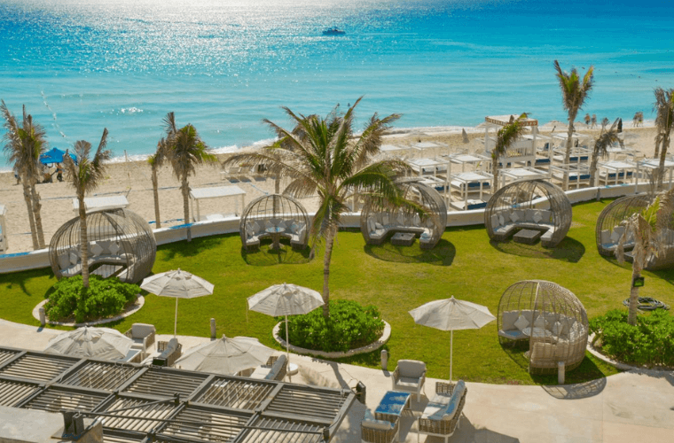 the garden and beach area at Sandos Cancun with palm trees and the Caribbean Sea in the background 
