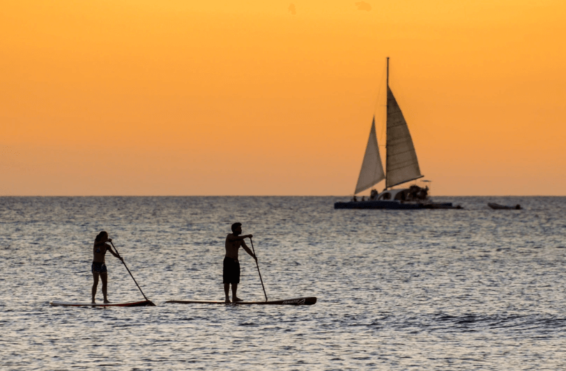 a couple paddleboarding with a yacht in the background 
