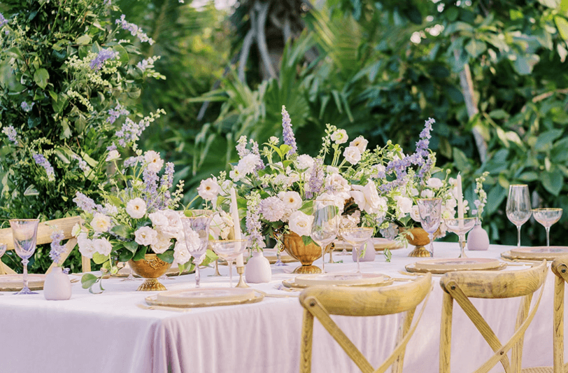 a table set for a wedding with flowers and glasses against a tropical green backdrop