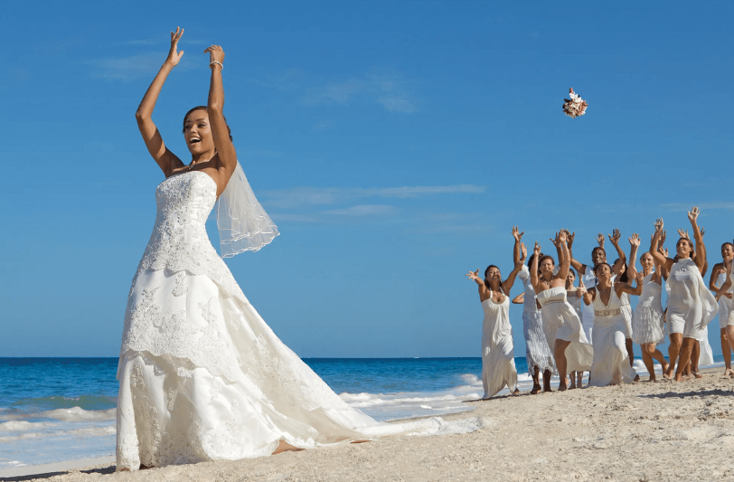 a bride tossing her bouquet to her bridal party on the beach 