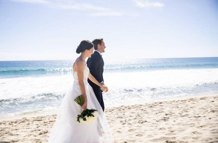 a wedding couple walking along the beach hand in hand 