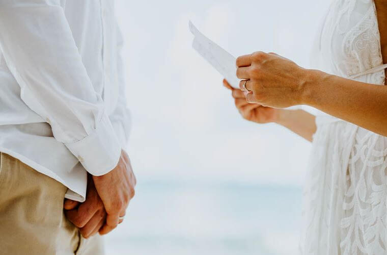 the hands of bride and groom with the bride holding a sheet of paper 