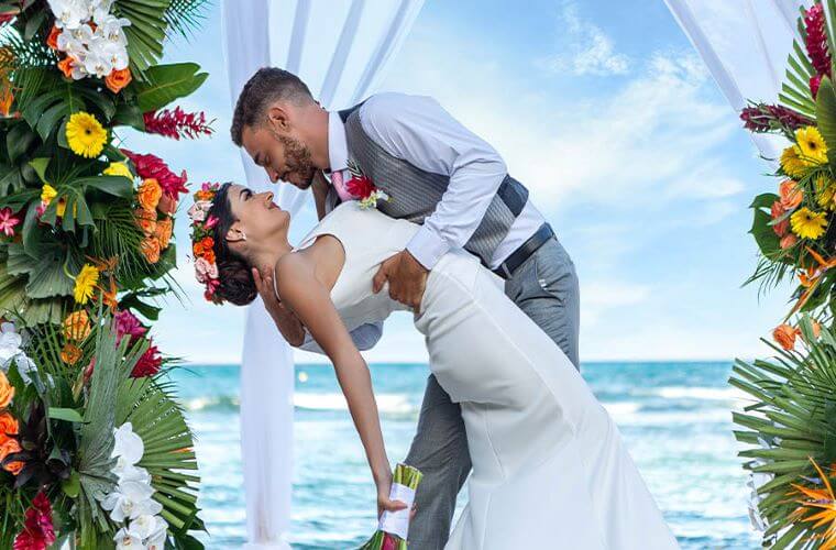 a bride and groom surrounded by flowers with a background of the Caribbean Sea 